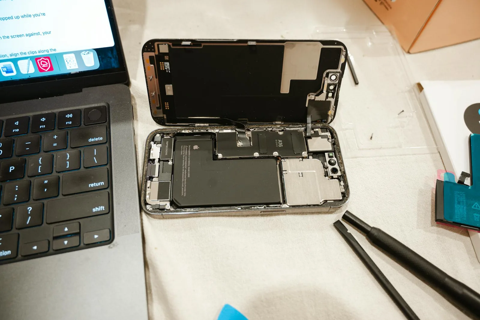 Smartphone-Reparatur mit Werkzeug und Laptop als Beispiel für Akku- oder Bauteiltausch