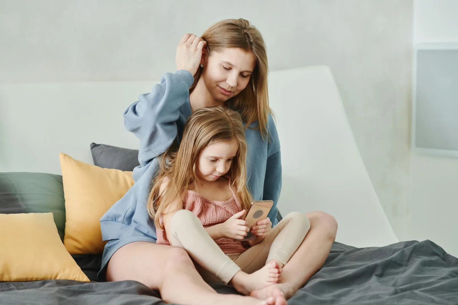 Kind mit Smartphone neben Mutter als Symbol für begleitete und sichere Handynutzung