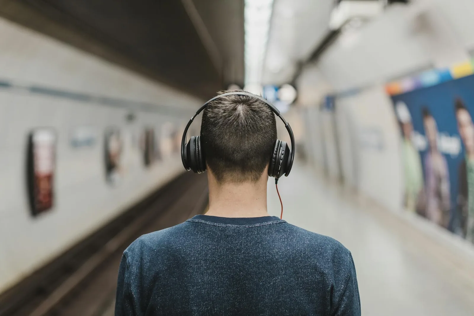 Mann mit Kopfhörern an einer Bahnstrecke als Beispiel für Podcast-Hören unterwegs und offline
