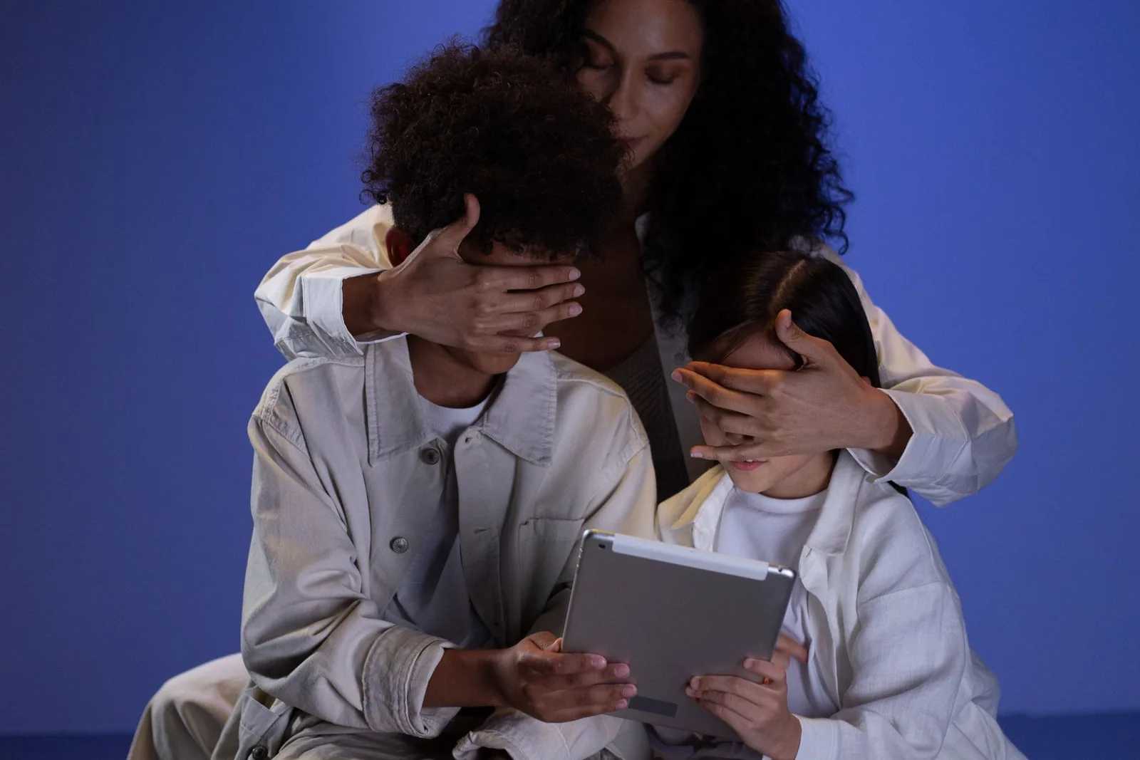 Mutter hält Kindern die Augen vor dem Tablet zu als Symbol für ungeeignete Online-Inhalte
